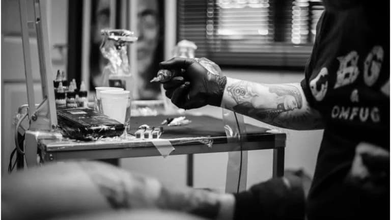 Tattoo artist in black gloves loading the machine at the studio station, in black and white